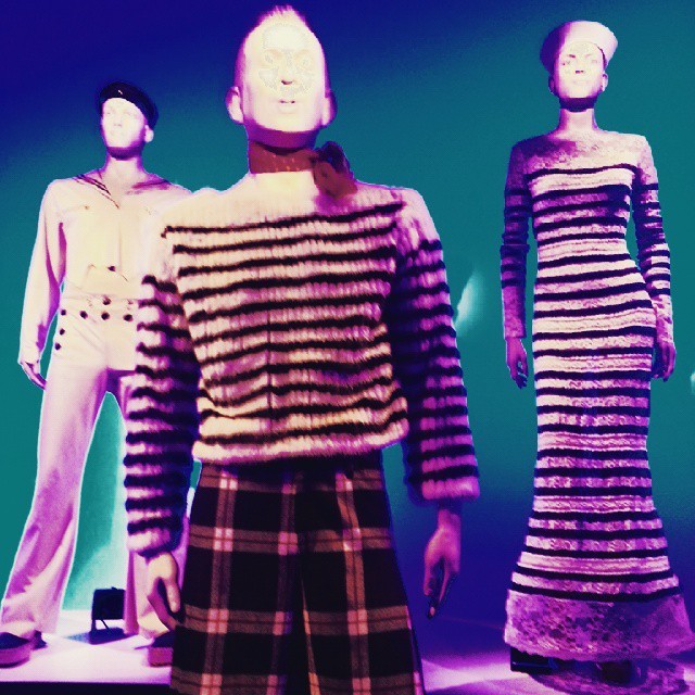 Purple light shines on three slender mannequins wearing sailor-themed clothing