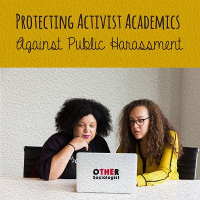 Two women of colour sit at a desk reading a laptop