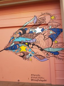 Street art against a salmon door. A beautiful blue, purple, yellow and black cosmic scene shows dogs, stars and other non-descriptfigures