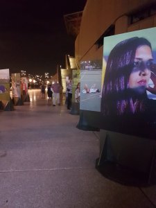 In the foreground is a large photo of a woman of colour from the Middle East. She is holding her hand to her temple, with shadows across her face. In the background is various other large photographs of young women