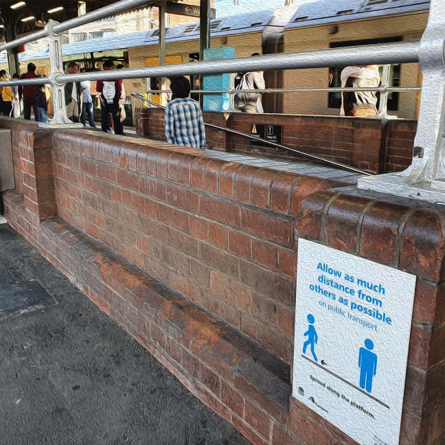 A busy Sydney train station in the background. A COVID-19 sign in the foreground reminds passangers to keep social distancing