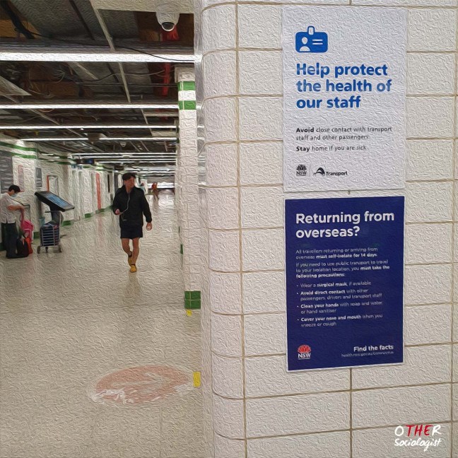 A person walks in the distance inside Central Station in Sydney. Two COVID posters say: 1 "help protect staff," and 2) "returning from overseas?"