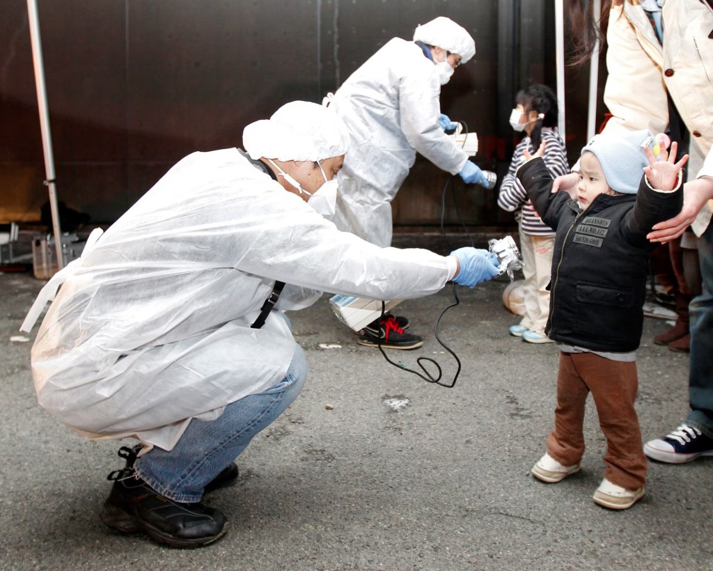 A man in white scrubs runs a devices in front of a child, who has their arms up