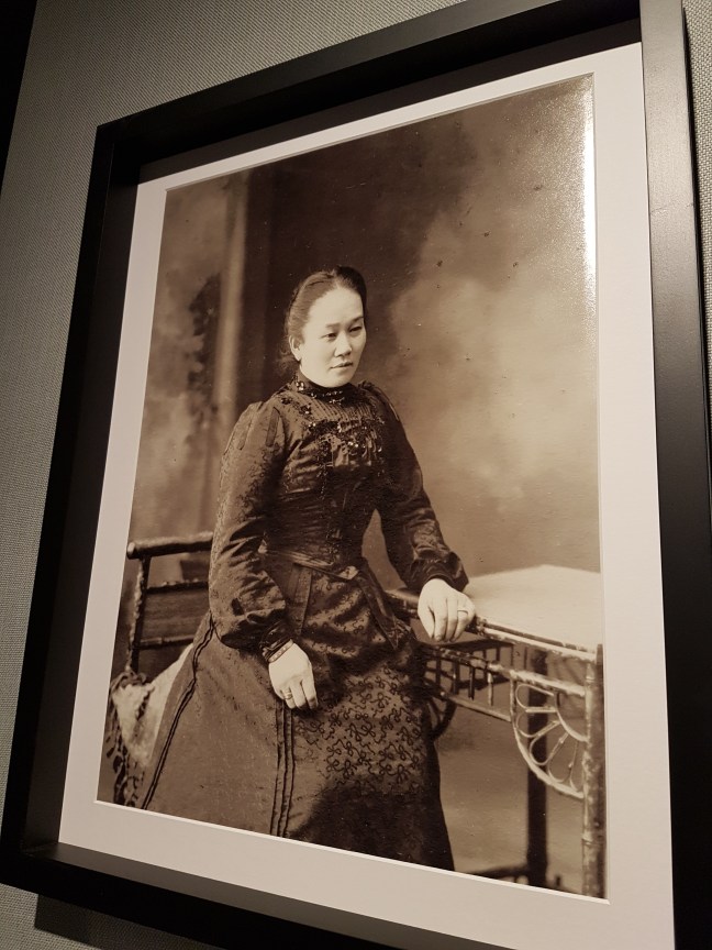 Chinese woman in setter colonial period dress sits to the side