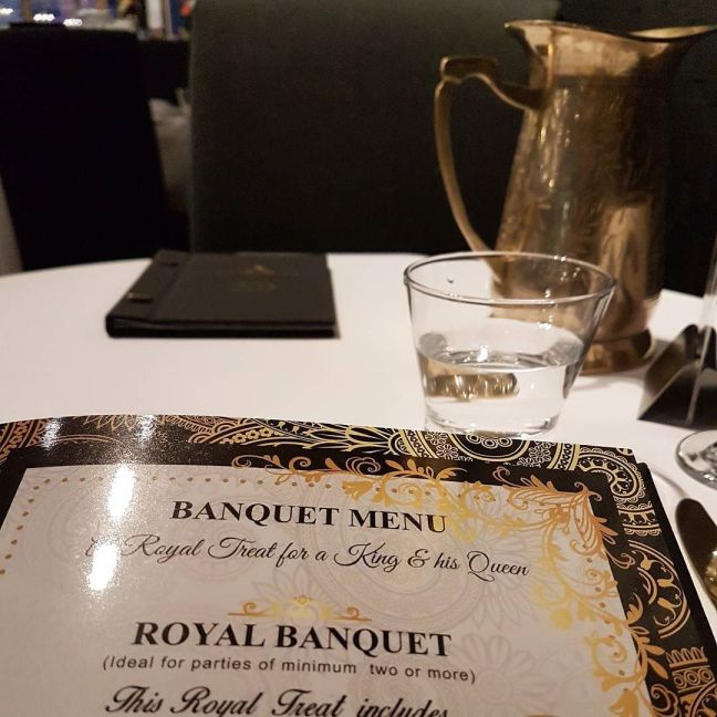 Table with a water jug and glass, and a banquet menu that reads: A royal treat for a King and his Queen
