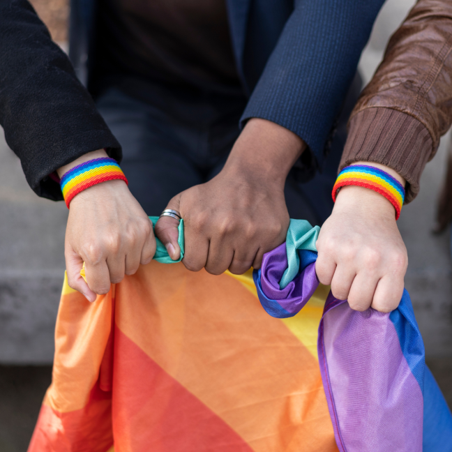 Three hands hold the Pride flag