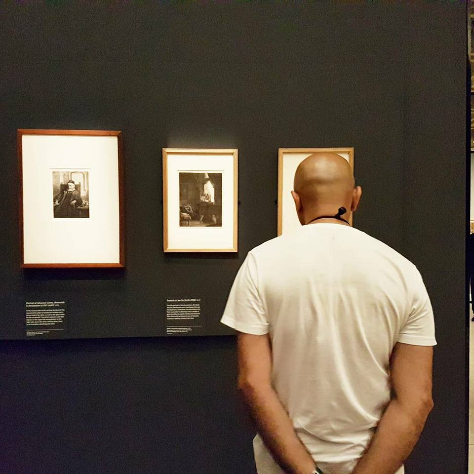 A bald man stares closely at photographs of Rembrandt