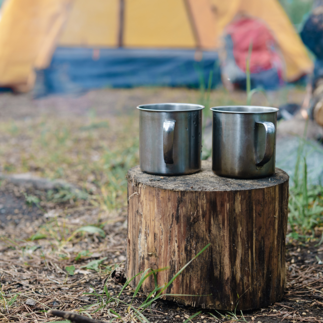 Two metal cups resting on a log, with a tent in the background