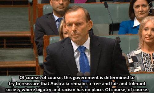 Tony Abbott arguing in Parliament. He is a white man with thinning brown hair. he wears a black suit. He say: Of course, of course, this government is determined to try to reaassure that Australia remains a free and fiar and tolerant society where bigotry and racism has no place. Of course, of course