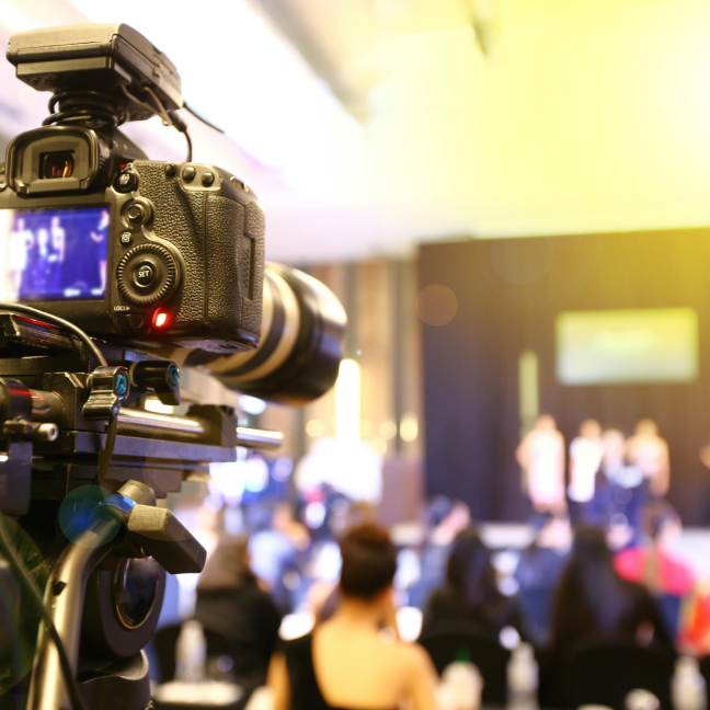A camera is pointed at a crowd and stage, with the background blurry