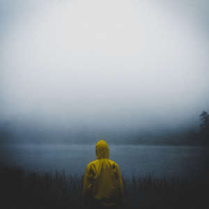 Child in raincoat seen from behind, staring into a foggy lake in Jawa Timur, Indonesia