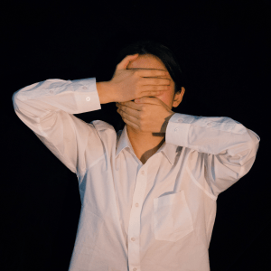 White woman wearing a white shirt covers her eyes and mouth with her hands